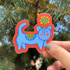 Colorful sticker of a blue creature with a red border held in front of green foliage